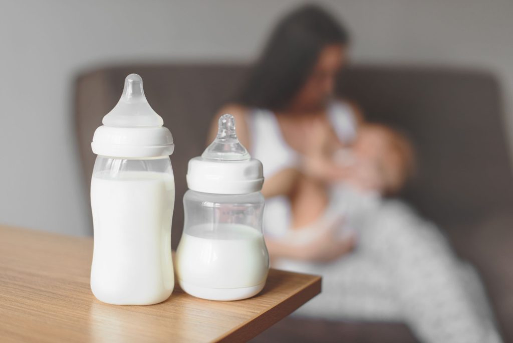 Mother breast feeding baby in the background of a picture where two bottles of breast milk are in focus of the photo
