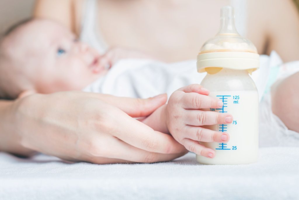 Mother holding baby whilst baby holds their bottle of breast milk
