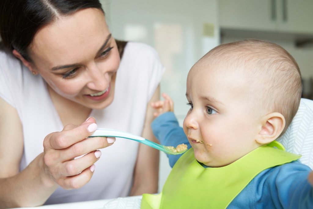 Mum spoon-feeding baby with a big smile on her face 