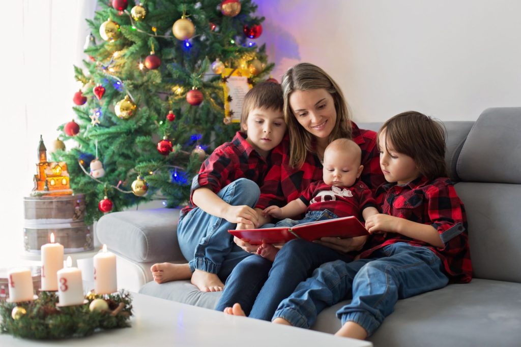 Mum and her children sat by Christmas tree reading a book