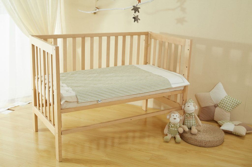 Wooden baby cot bed with teddys and cushions beside it on the ground