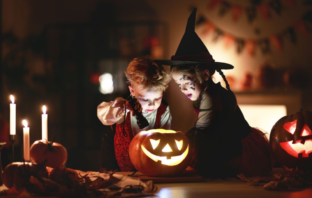 Little boy dressed up as a vampire and little girl dressed up as a witch. Both are looking over a pumpkin