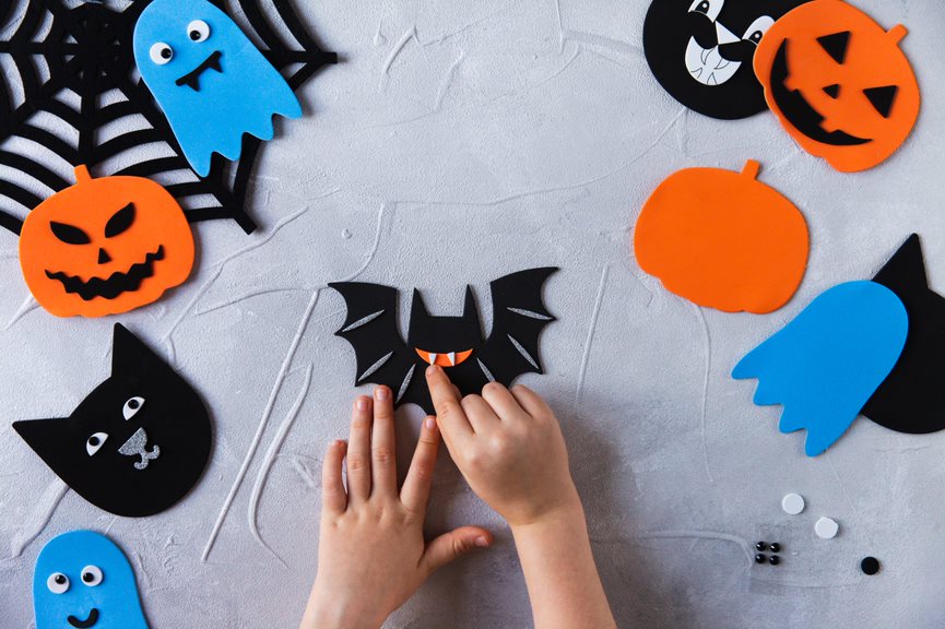 Child's hand can be seen to be making Halloween pumpkins and bats out of arts and crafts