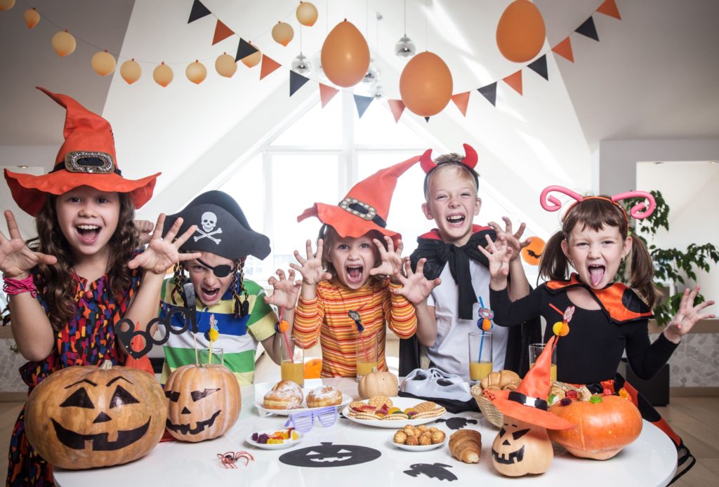 Children sat round the table at a Halloween party making scary faces whilst dressed up as witches, pirates and vampires