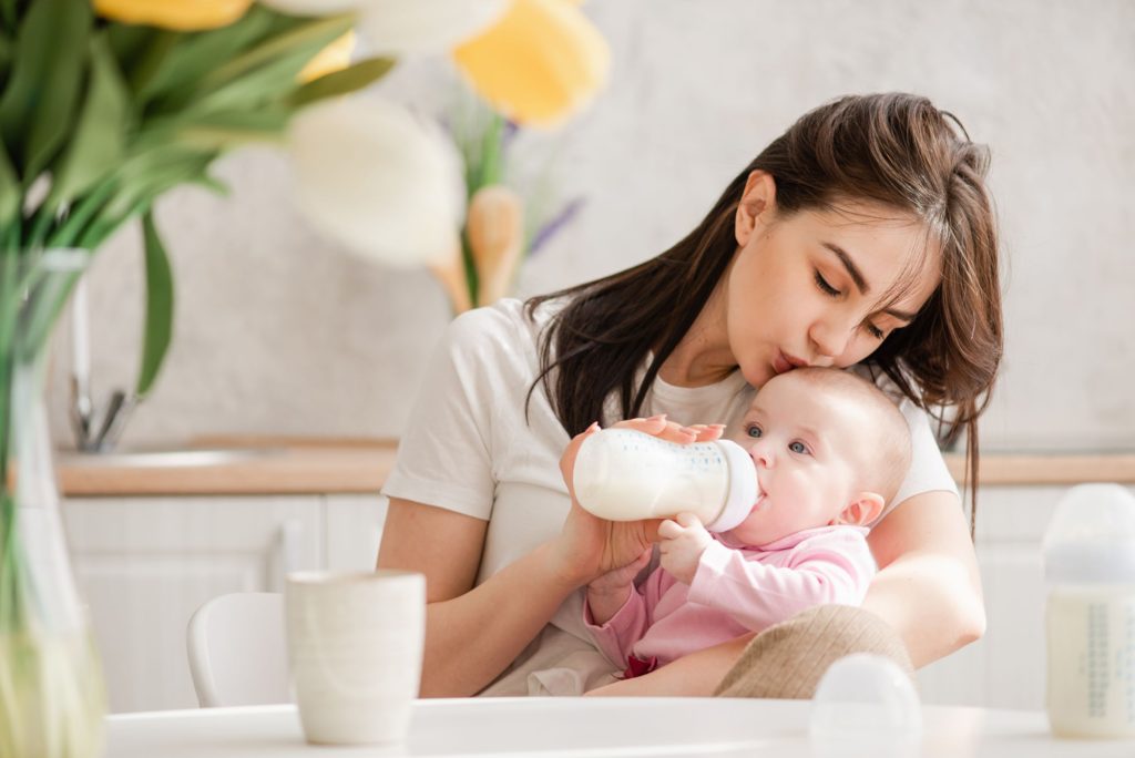 Mother kissing baby on head whilst feeding baby milk from a bottle 