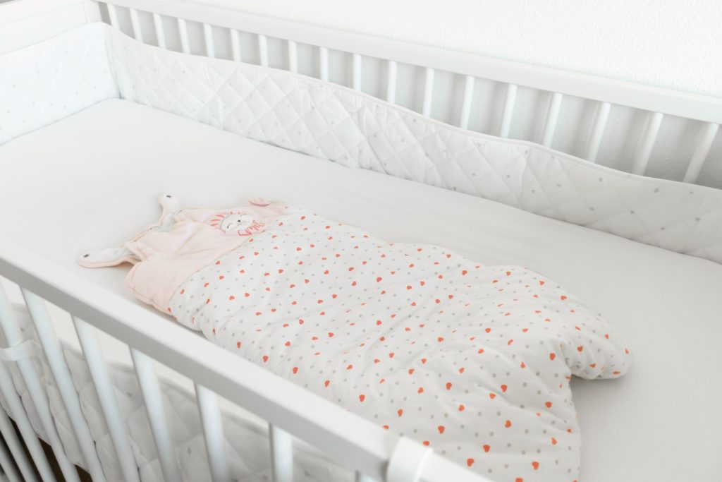 Pink and white baby sleeping bag placed in a cot