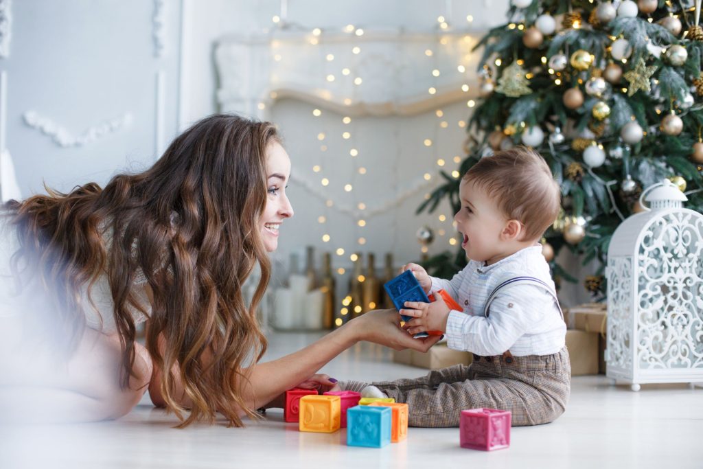 Happy mum and baby playing with building blocks in front of the Christmas tree