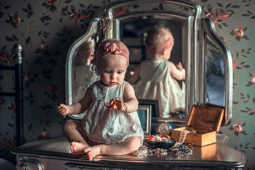 Little girl sat on vanity table looking at jewellery 