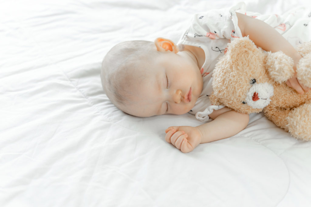 Baby sleeping whilst cuddling cute teddy