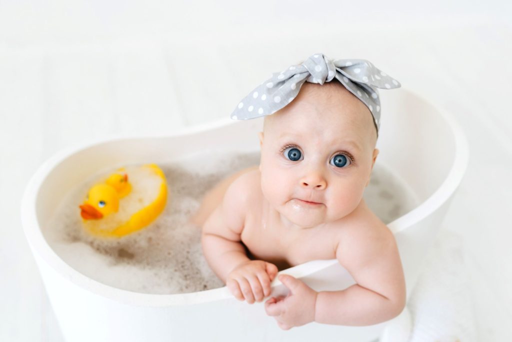 Baby with big blue eyes in a baby bath with rubber duck