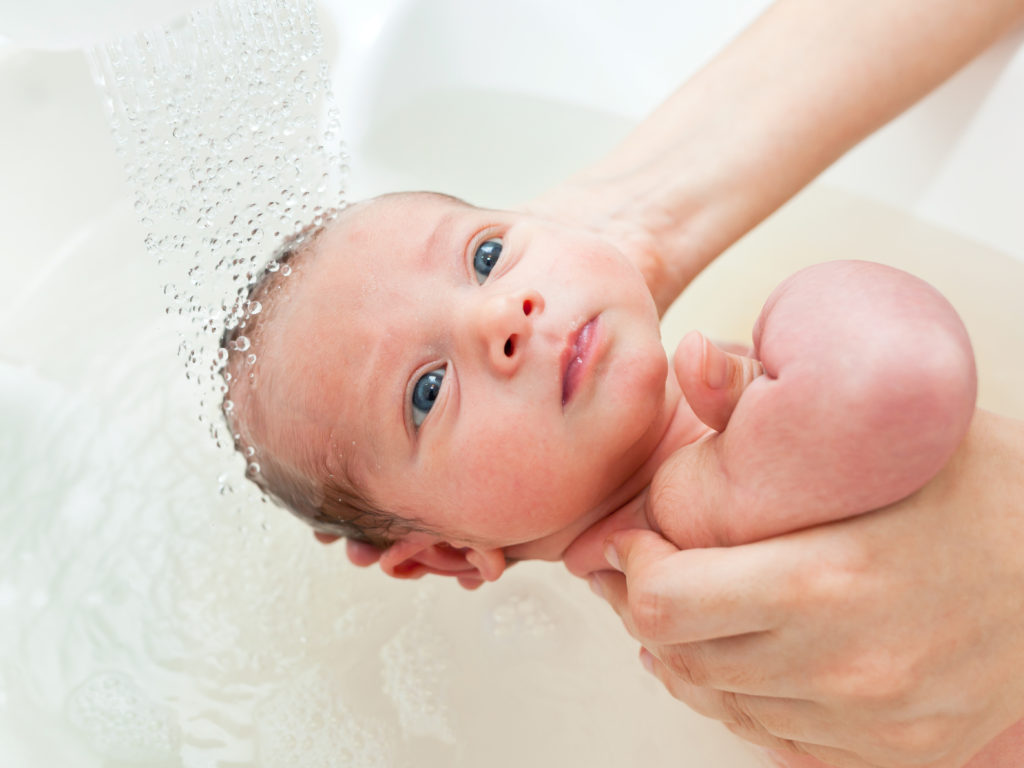 Newborn baby being held by the head by parent in water