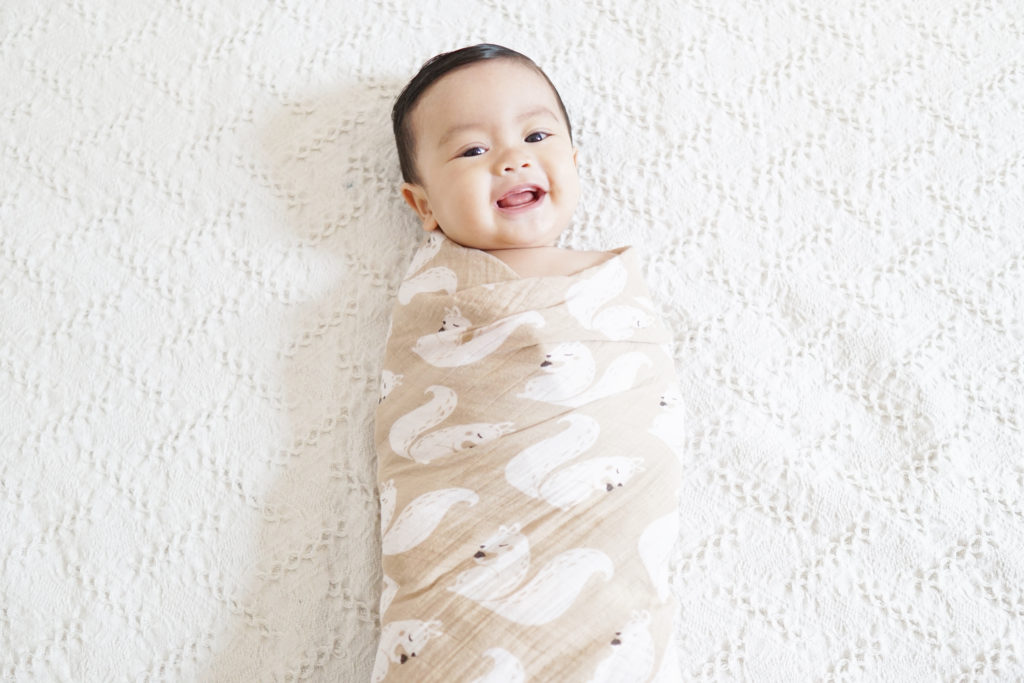 Cute baby laughing and smiling whilst being swaddled
