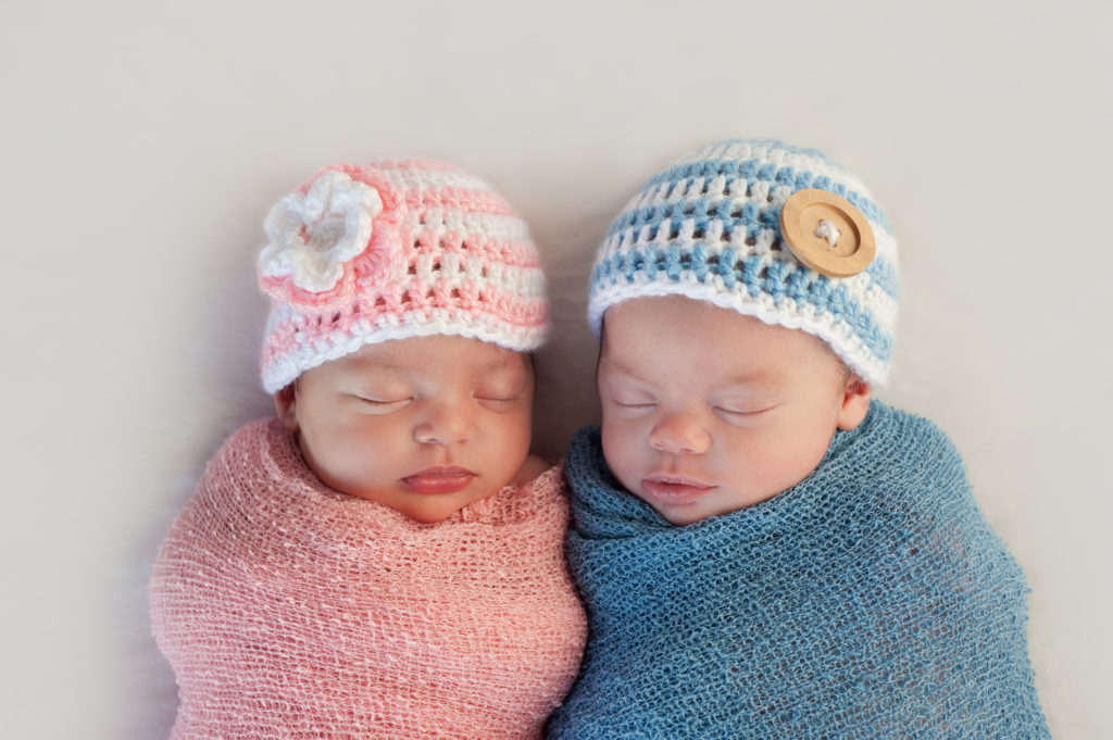 Twin girl and boy sleeping next to each other in pink and blue swaddles