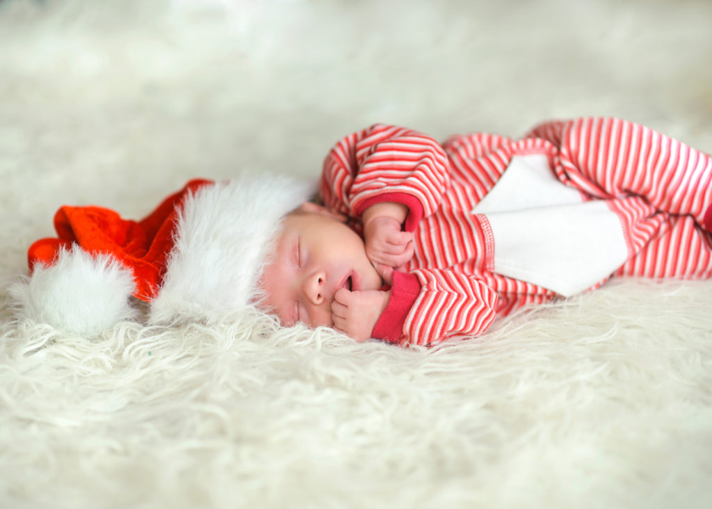 newborn baby in red and white stripe onesie, wearing a Christmas Santa hat whilst asleep