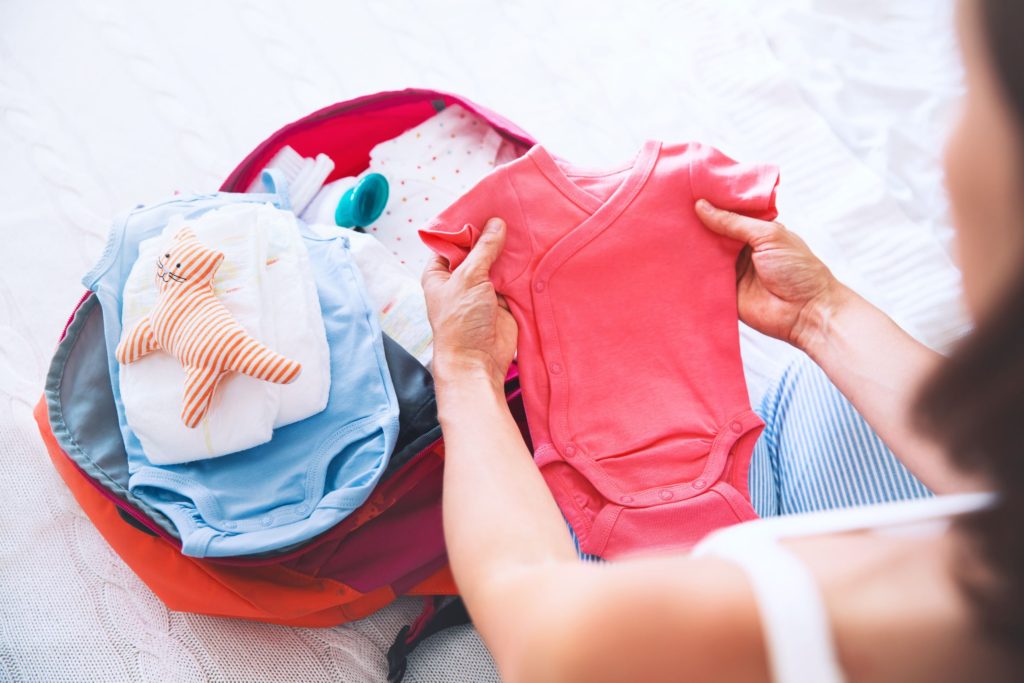 Woman packing hospital bag whilst holding baby onesies