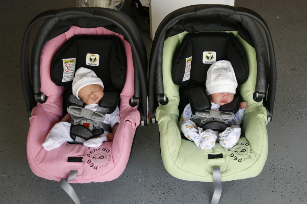 Twin babies in pink and green car seats