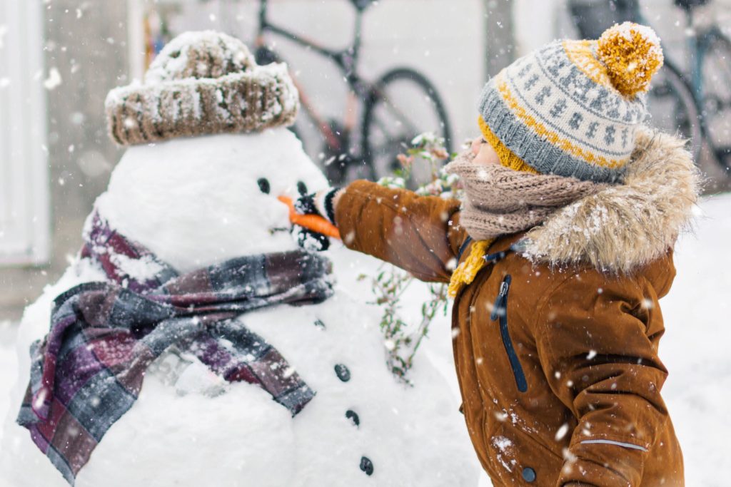 Child outside in winter touching the snowman's face