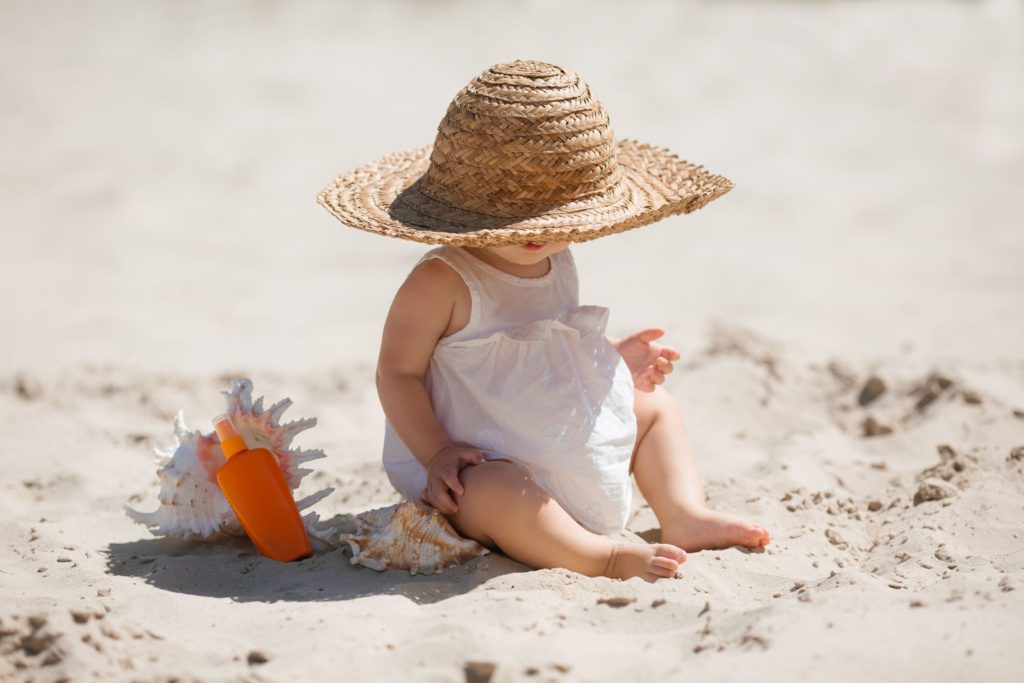 Little girl with sunhat sat on sandy beach