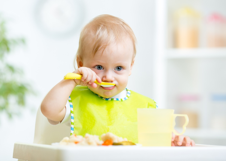 baby in a highchair and yellow bib feeding themselves