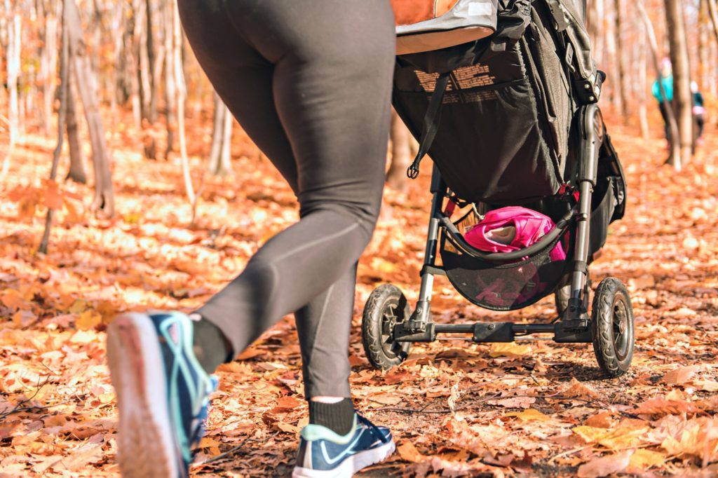 Up close image of mum running in leaves with a pushchair 