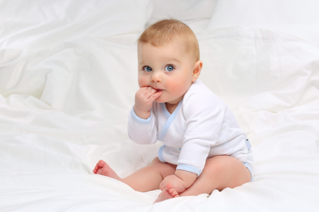 Cute baby with big blue eyes sucking on their fingers