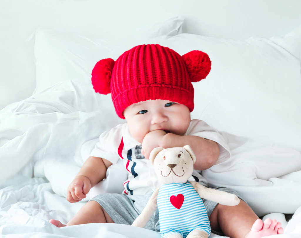 Baby sucking their thumb with a red woolly hat on
