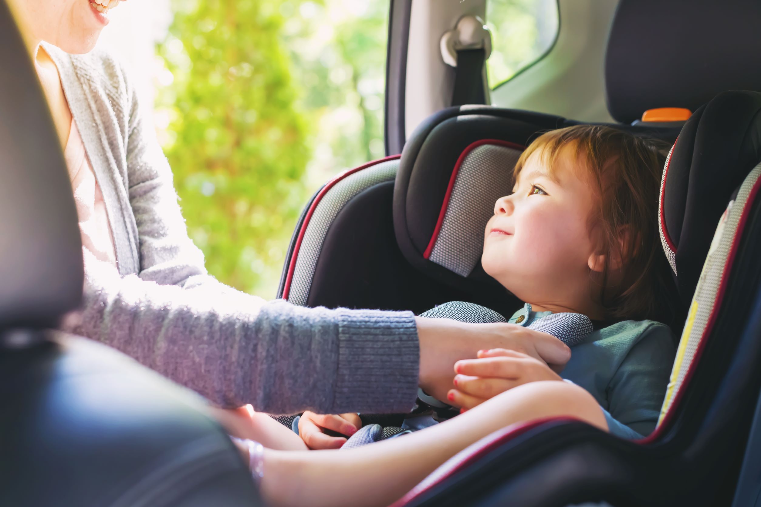 Child smiling back at mum whilst being buckled into car seat