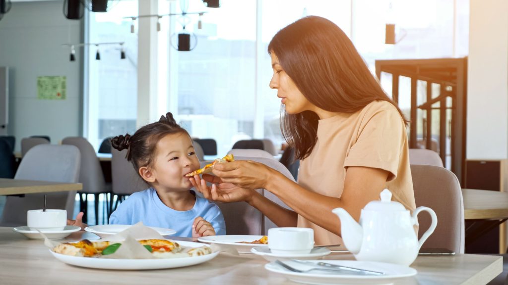 A mother feeding her toddler some pizza