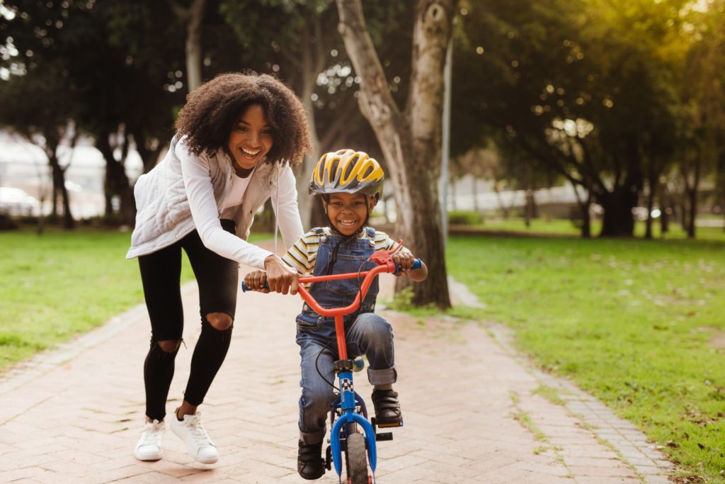 a child riding a bike, supported by his mother