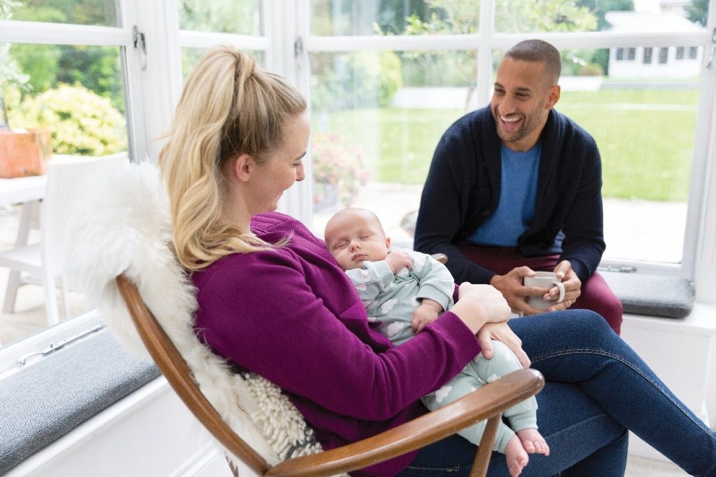 Mum holding sleeping baby whilst dad smiles lovingly