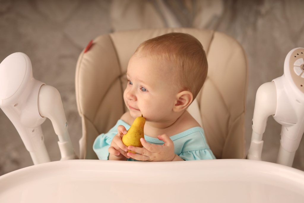 Baby smiling whilst holding a pear in their hand