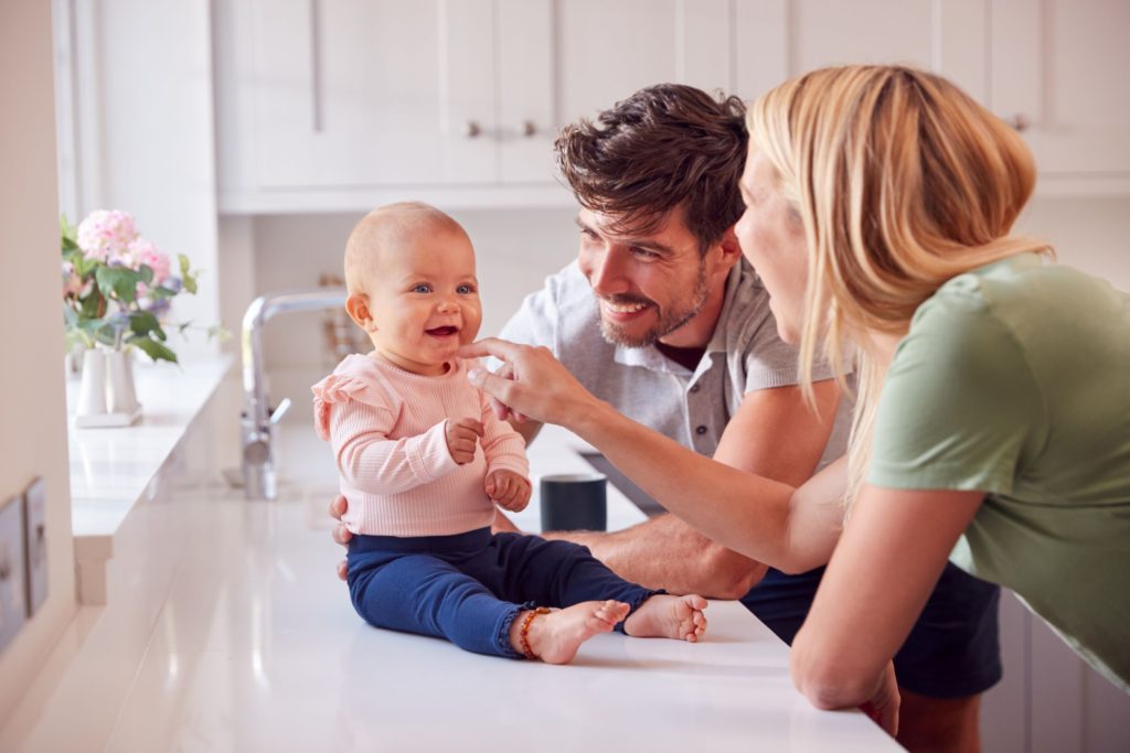 Mum and dad having fun and smiling whilst baby sits on kitchen counter