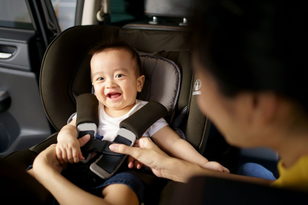 Little boy smiling whilst his dad clips him into his car seat