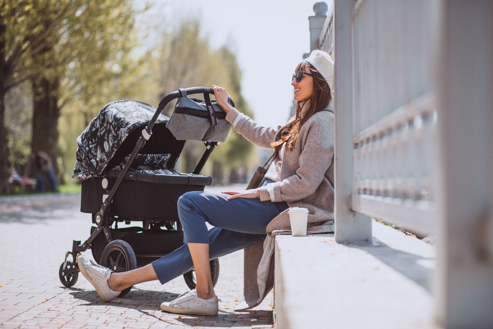 Young,Mother,Walking,With,Baby,Carriage,In,Park